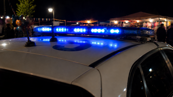 Ρεαλιστική συμβολική εικόνα με κοντινό πλάνο σε περιπολικό και αναμμένο φάρο, κατά τη διάρκεια νυχτερινού πανηγυριού, για χρήση σε άρθρο σχετικό με καταγγελία που προκάλεσε ανησυχία στο Δισπηλιό. Η εικόνα έχει δημιουργηθεί με τη χρήση τεχνητής νοημοσύνης.